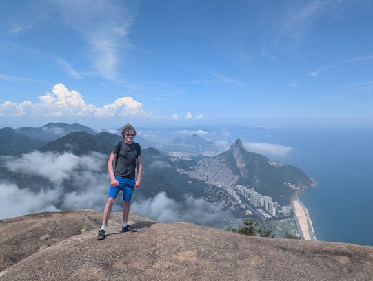 Moritz standing on the summit of Pedra de Gávea with a panorama view of Rio de Janeiro in the background.